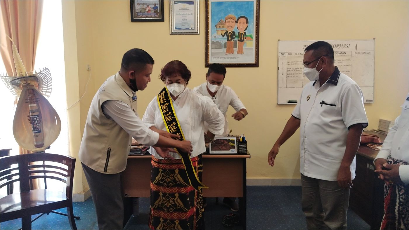 Ketua FTBM NTT Polikarpus Do memasangkan selempang, sebagai tanda pengukuhan Bupati Rote Ndao Paulina Haning-Bullu menjadi Bunda Baca Kabupaten Rote Ndao periode 2021-2025, di ruang kerja bupati, Sabtu (23/10/2021). Foto: Dok.ROOLNews